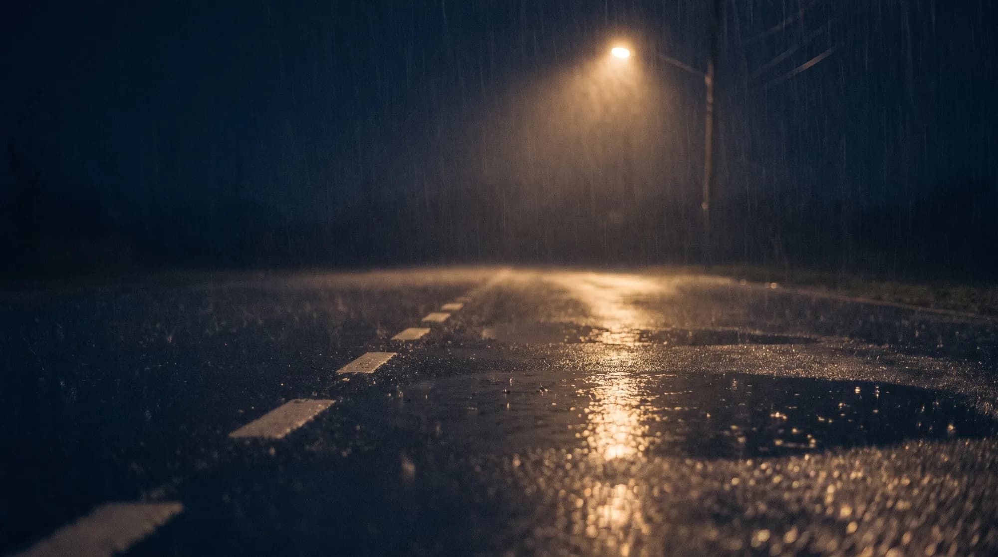 Nasse Fahrbahn bei Nacht, gestrichelte Mittellinie im Laternenlicht