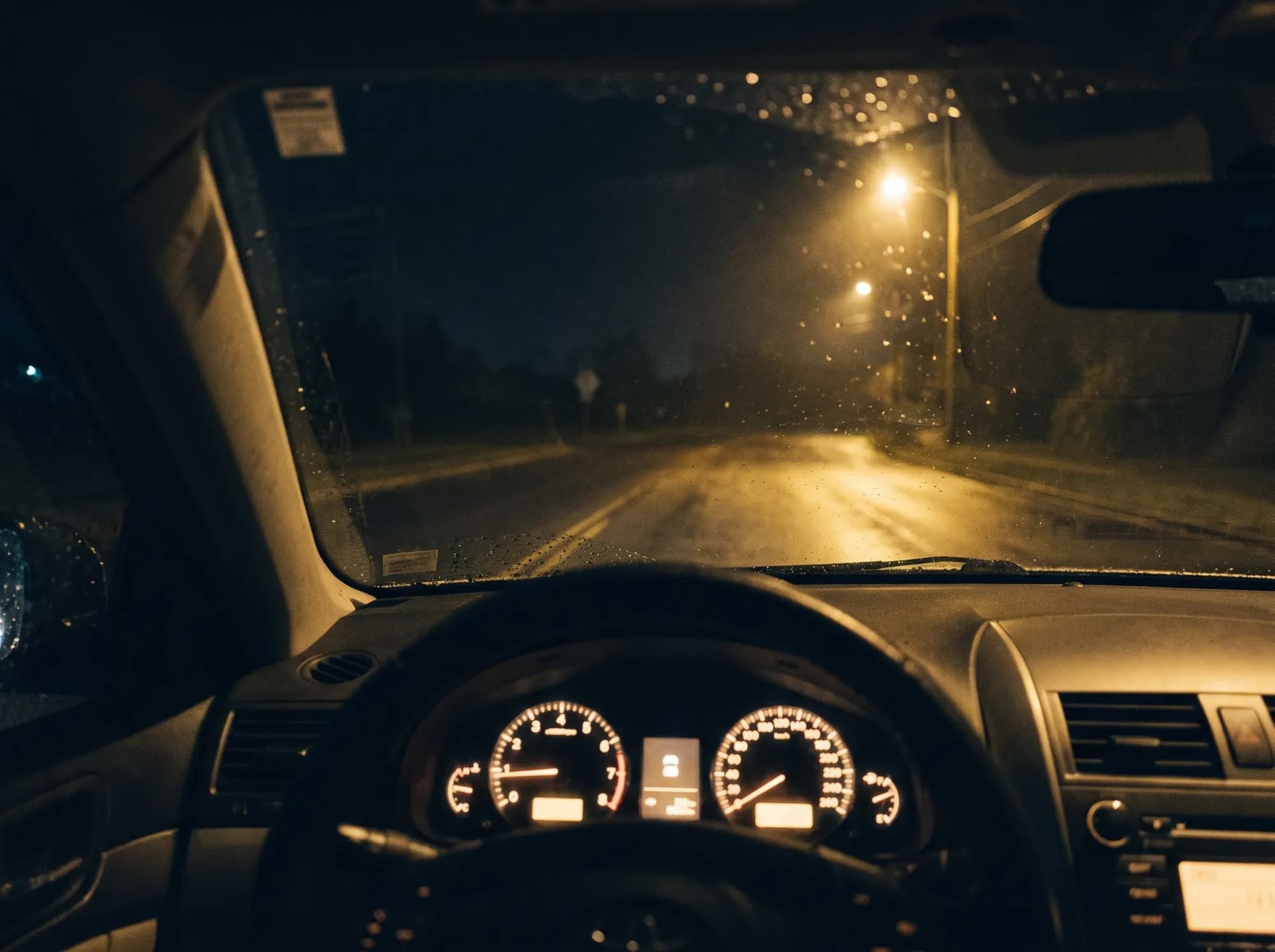 Blick vom Fahrersitz durch eine regennasse Windschutzscheibe auf eine leere Straße bei Nacht